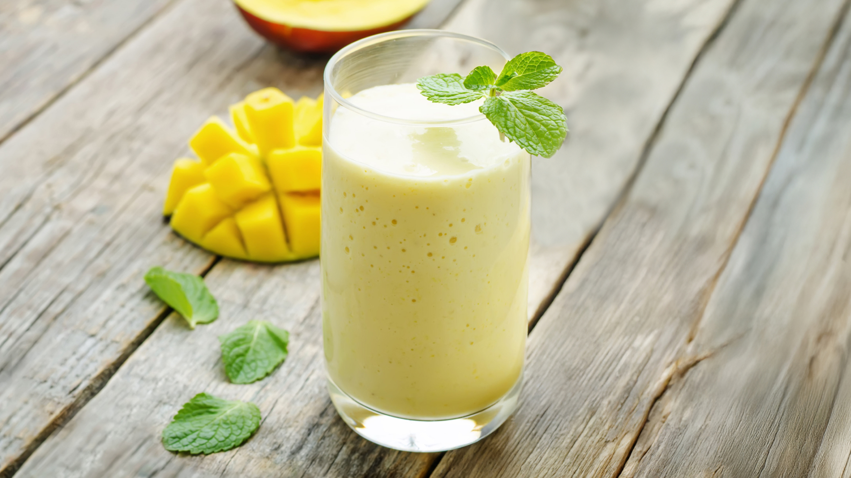 A glass of creamy yellow High-carb Banana Mango Smoothie from the Centr menu, decorated with mint leaves, is ready for drinking.