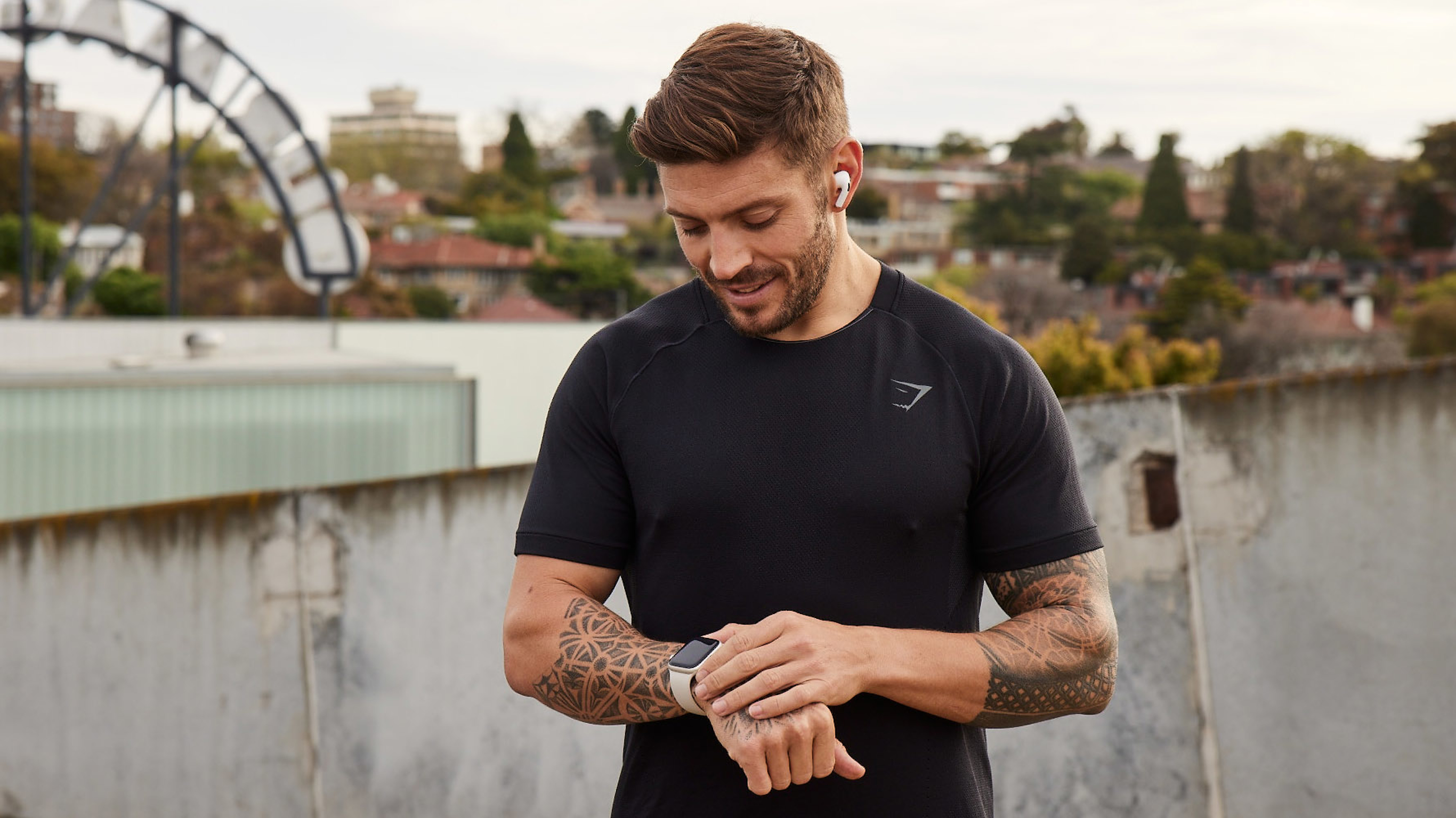 Centr trainer Luke Zocchi pauses to check his smartwatch while exercising outdoors in a cityscape.