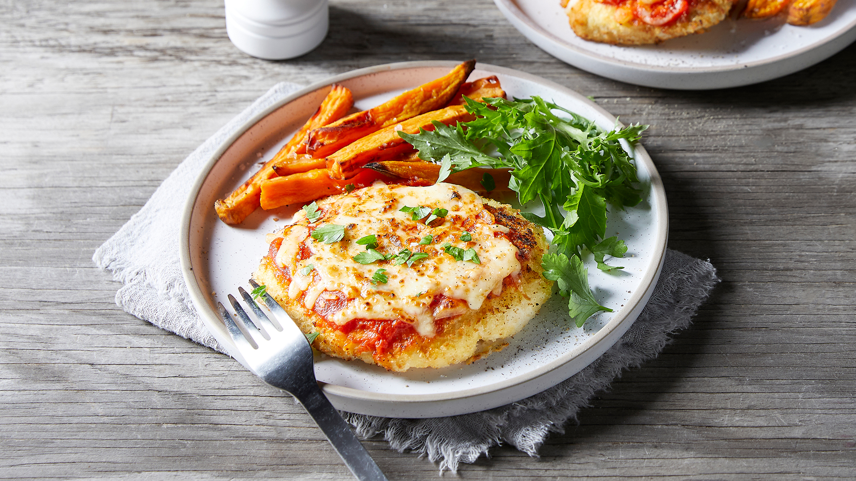 A plate of Centr's Easy Chicken Parmesan with Sweet Potato Fries and side of salad leaves is ready for eating