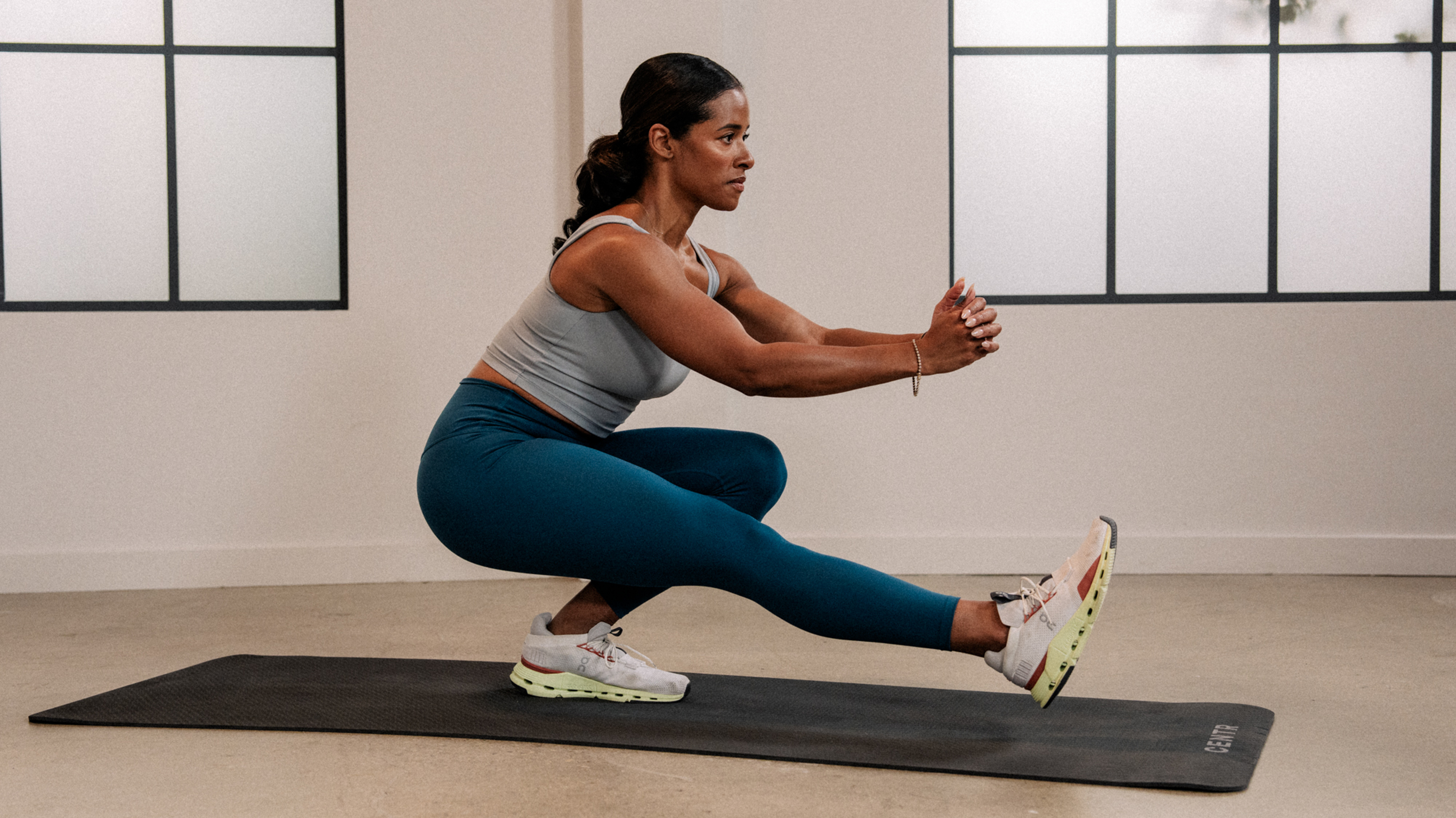 Ingrid Clay performs a pistol squat with her hands clasped in front of her chest.