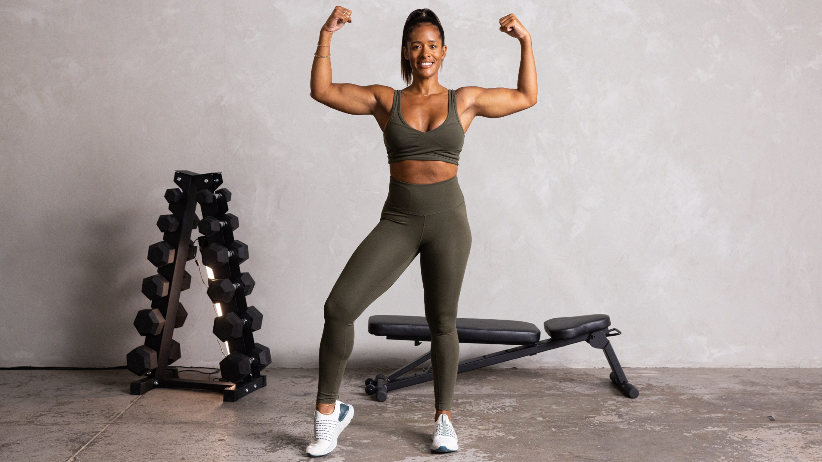 Ingrid Clay faces the camera and strikes a pose, flexing both arms in a raised lateral bicep curl