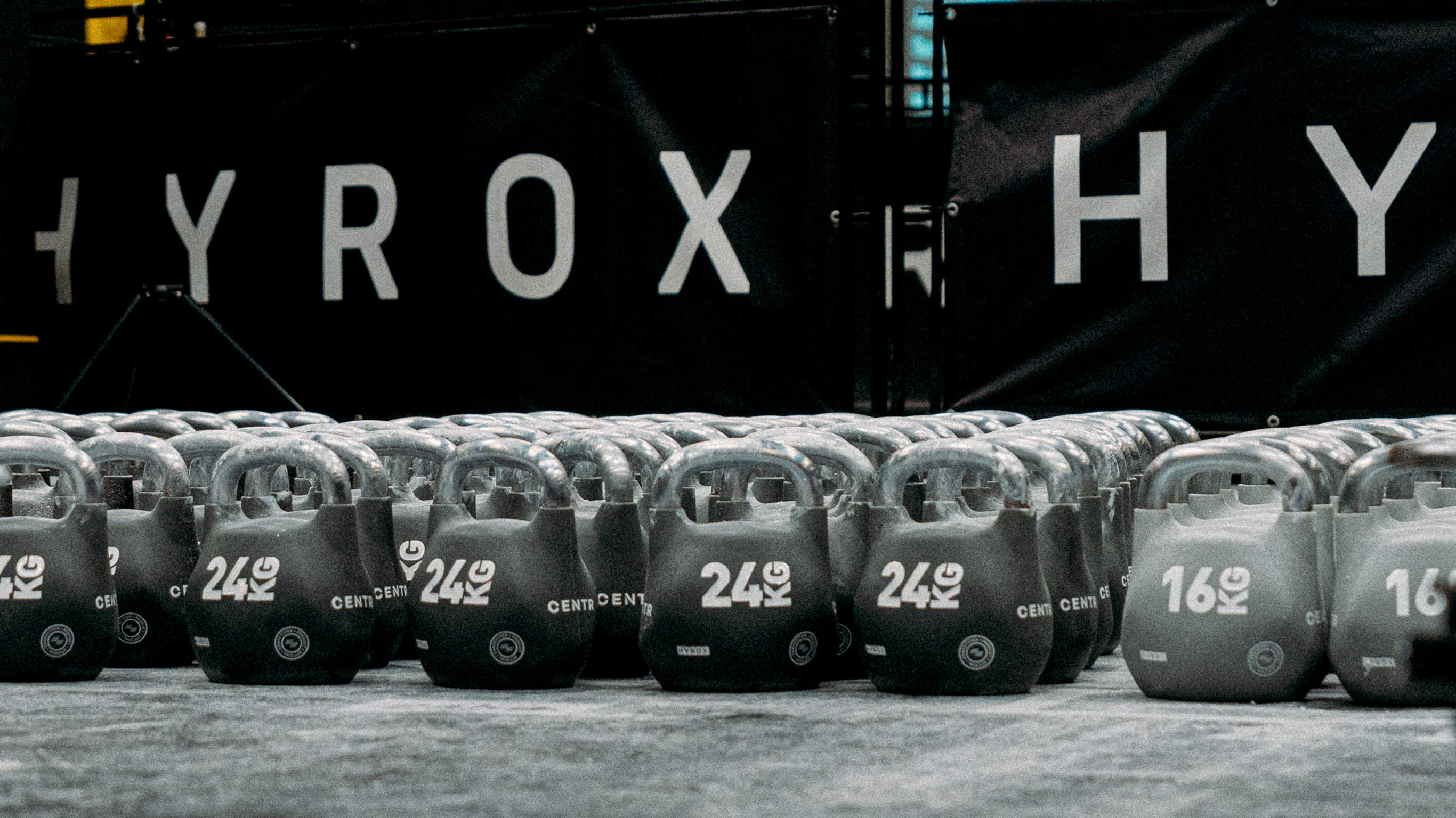 Rows of Centr 25 kilogram and 16 kilogram kettlebells are ready for competitors at a HYROX competition