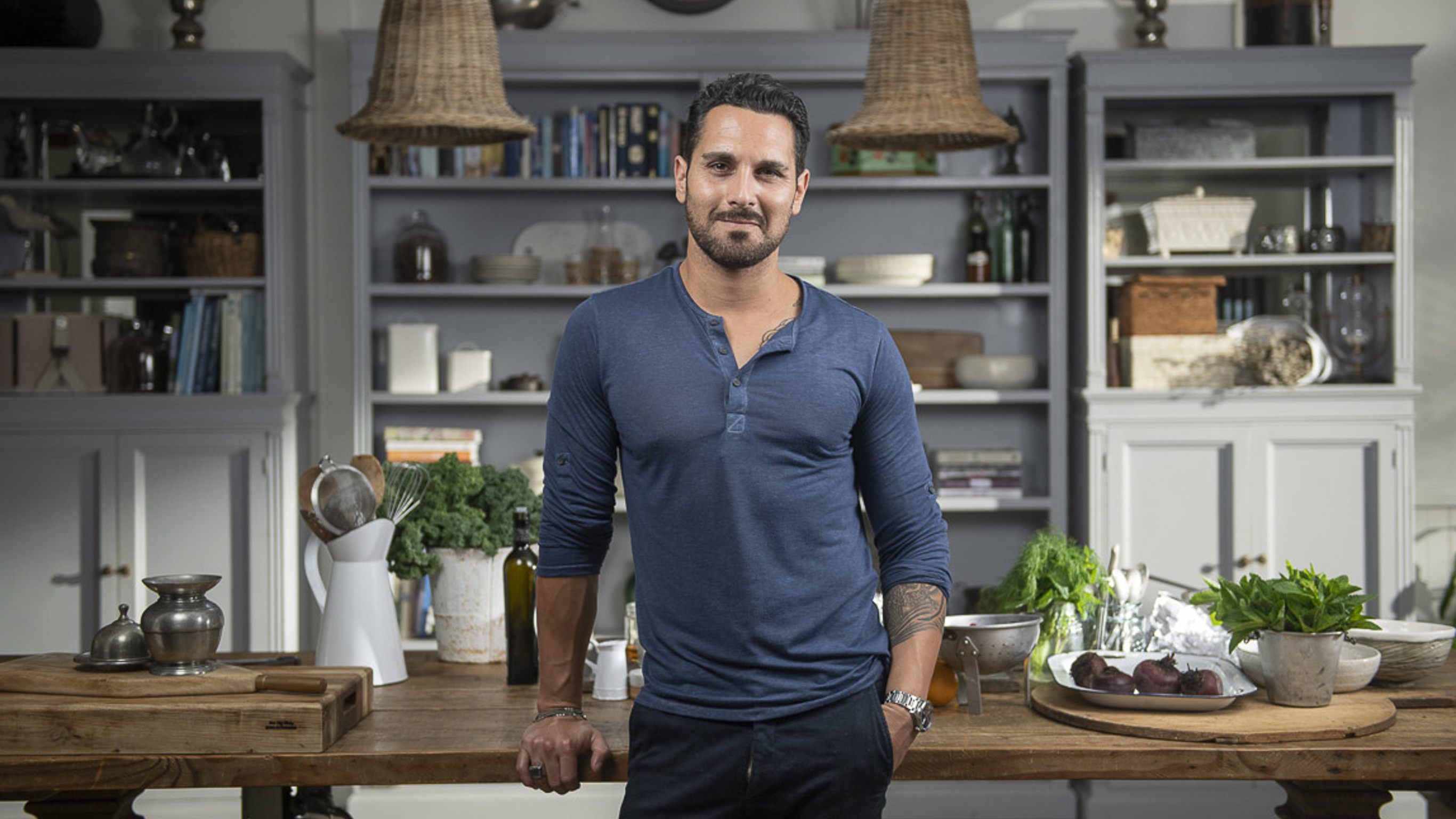 Sergio Perera stands against a large wooden table covered in produce and tools.
