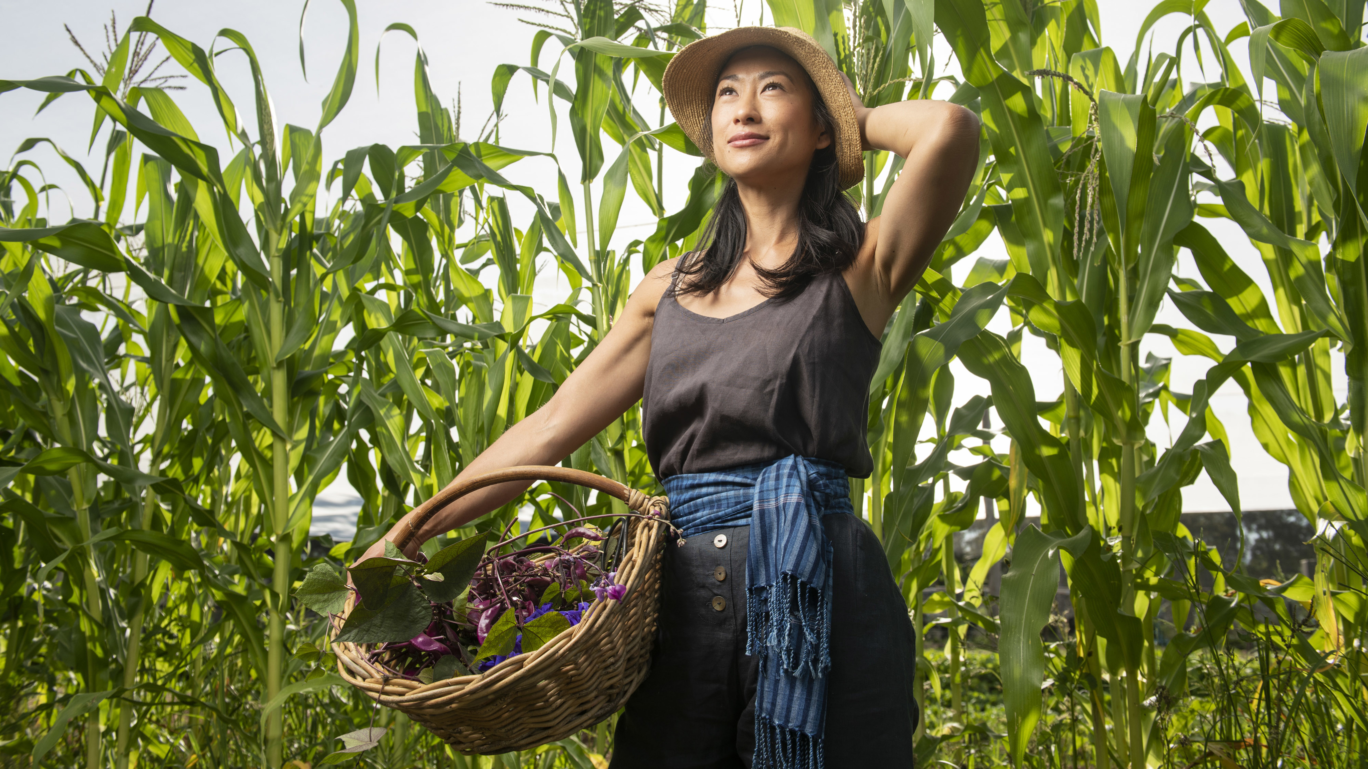 Palisa Anderson in a field, surrounded by tall green plants, holding a wicker basket.