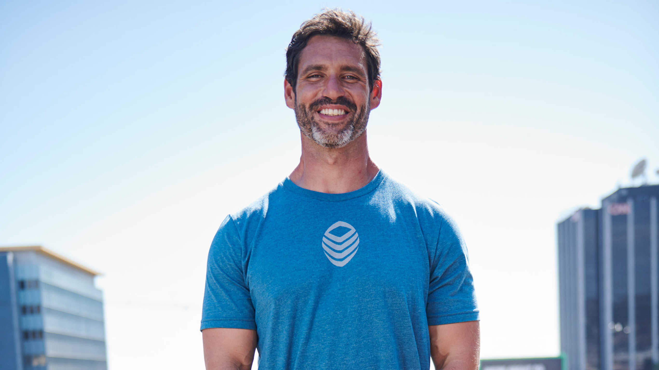 Dr. Eric Goodman, wearing a blue shirt, stands in the sun smiling.