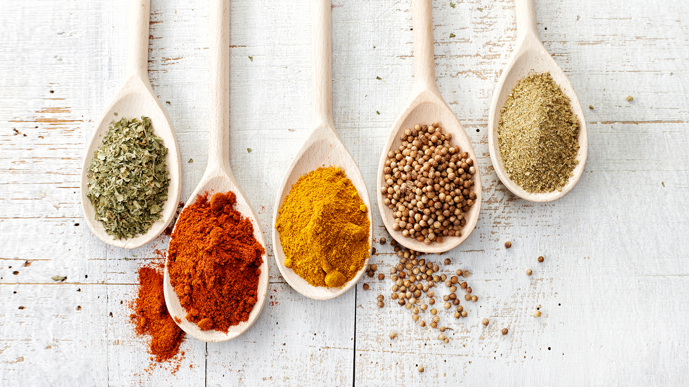 Five wooden spoons, each with a different spice or herb.