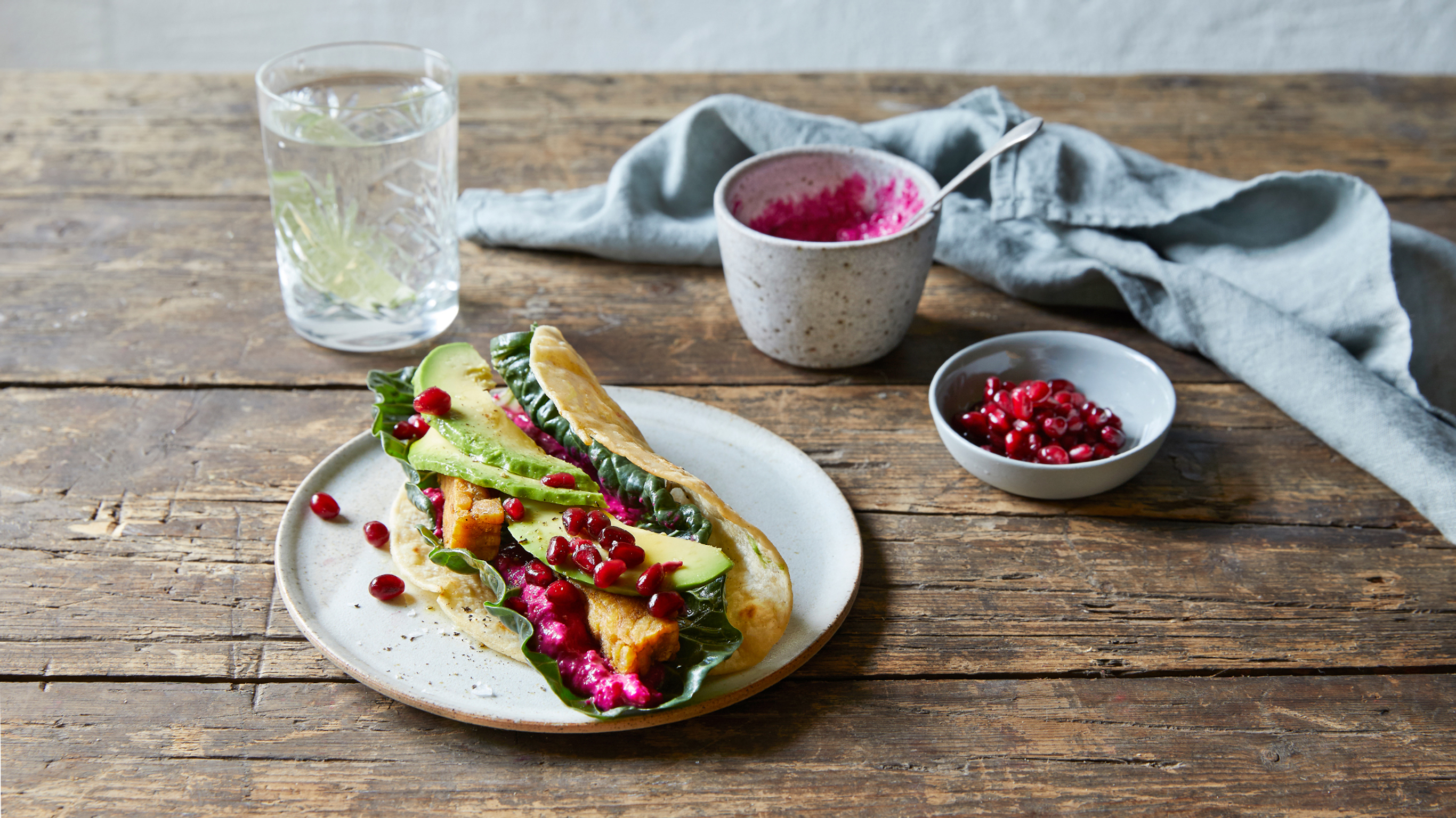 Centr's Tempeh Wrap with Pomegranate sits on a plate on a wooden table.