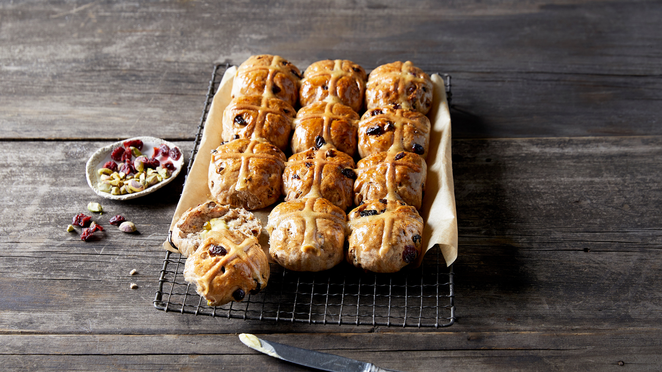 A dozen freshly baked Cranberry & Pistachio Hot Cross Buns from the Centr menu cool on a baking rack.