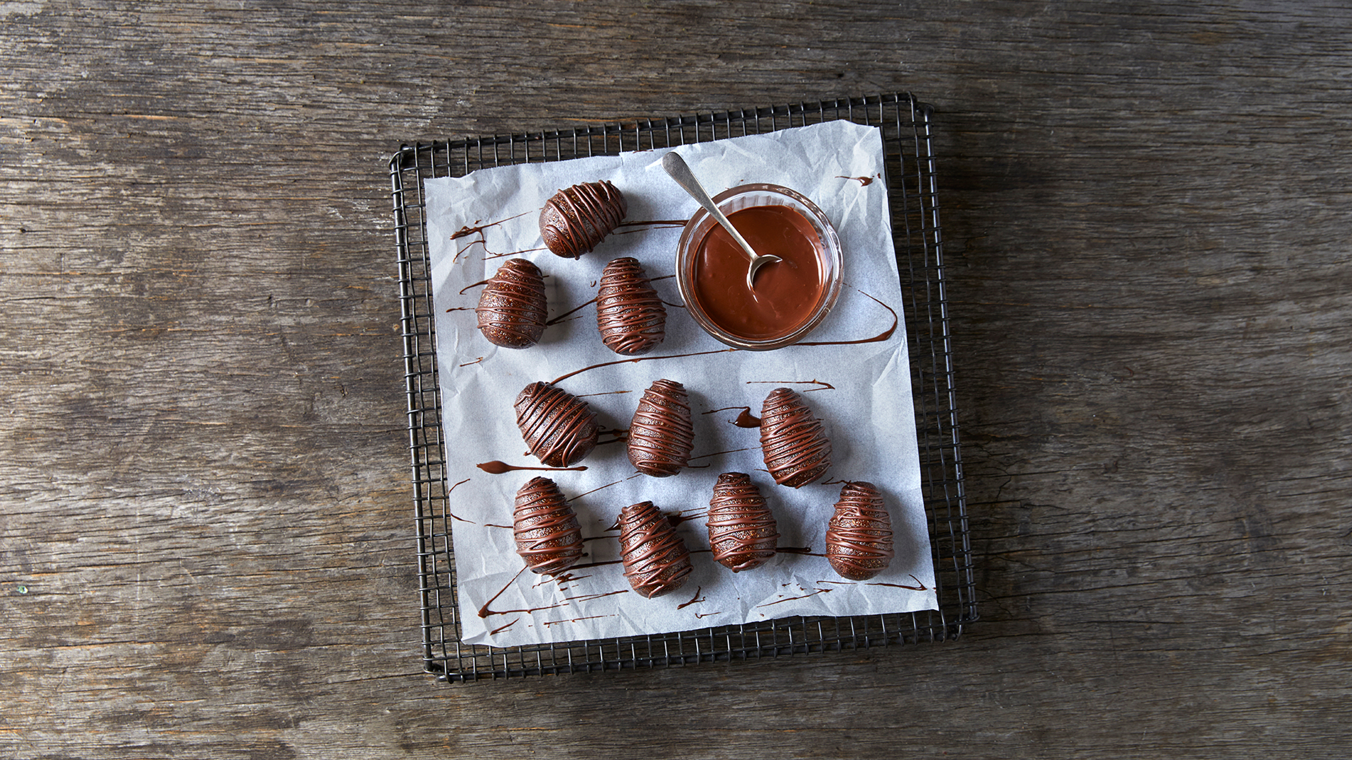Centr's Easter Egg Bliss Balls rest on a baking paper on a wire rack, with melted chocolate drizzled on them.
