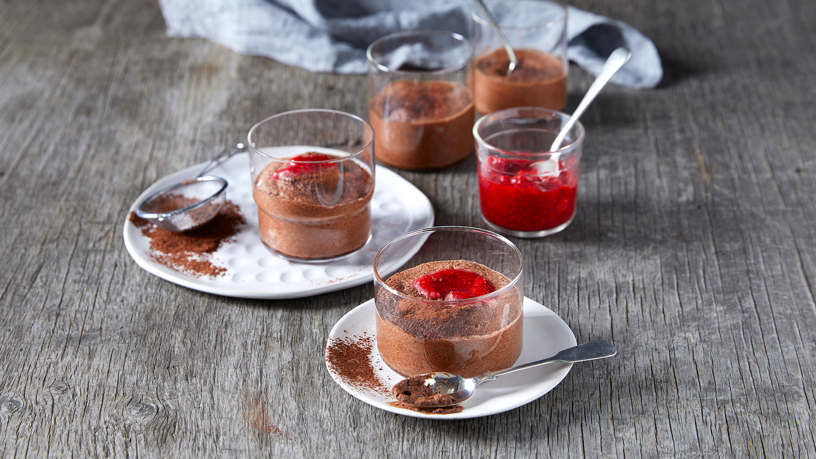 Four little glasses filled with Centr's Chocolate Raspberry Mousse are being decorated with mashed raspberries and dusted with cocoa powder.