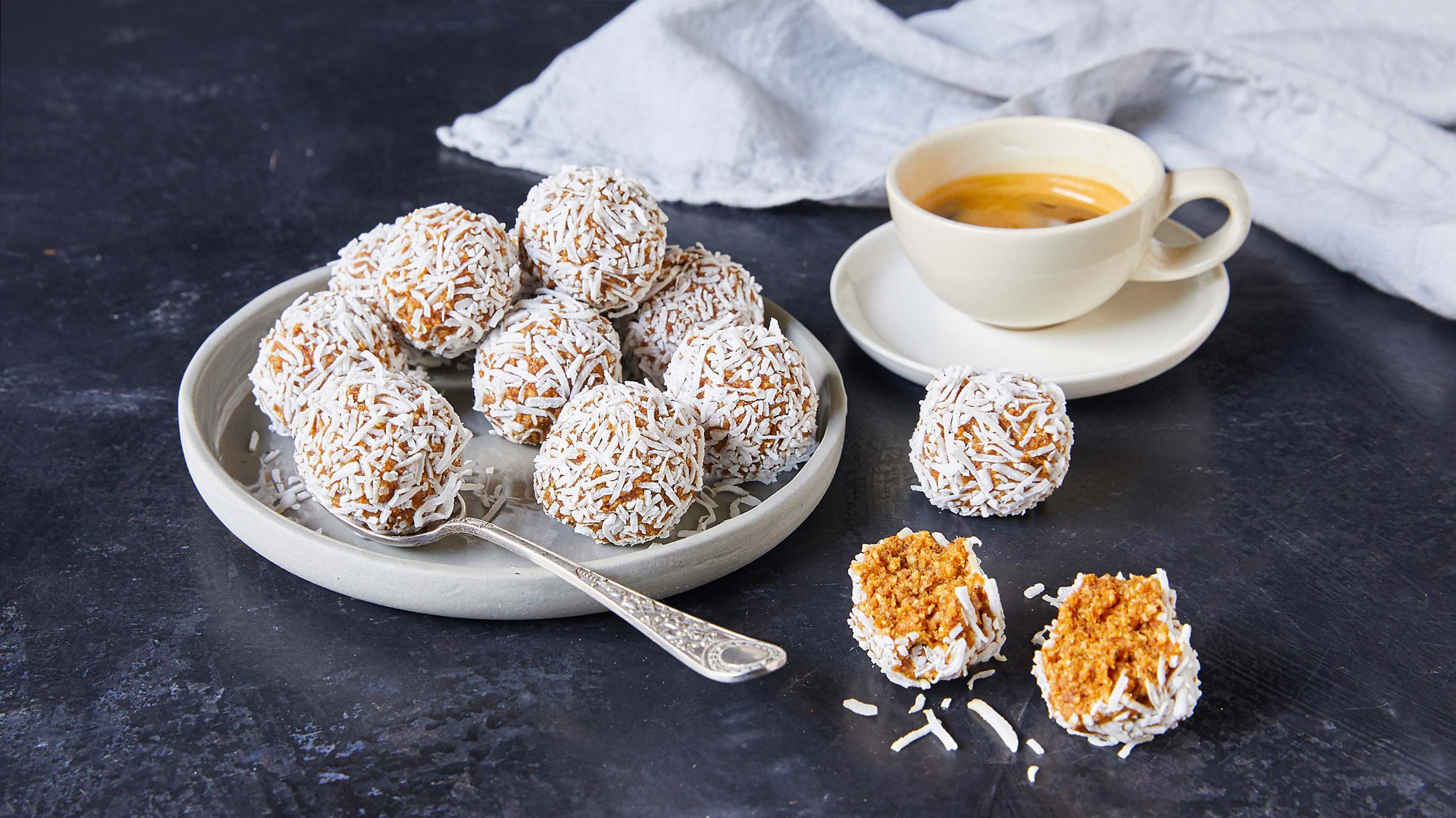 A plate with several coconut caramel bliss balls next to a cup of coffee.
