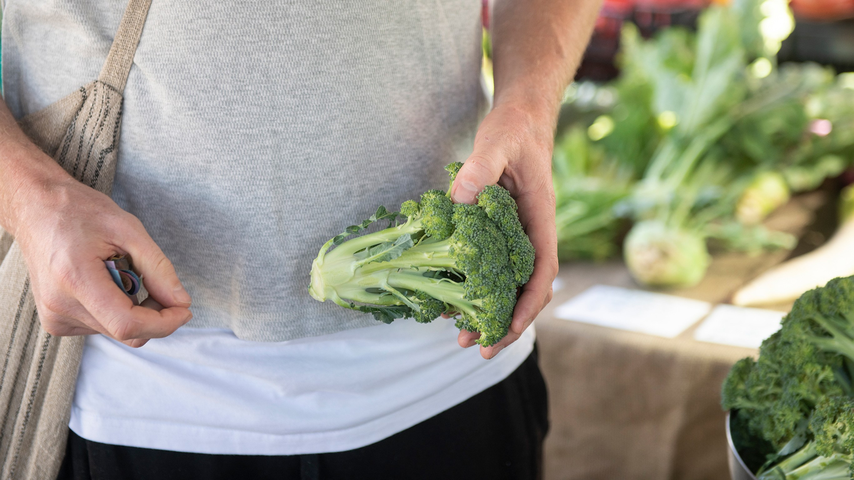 A close-up of a large head of broccoli held by a person shopping at a market.
