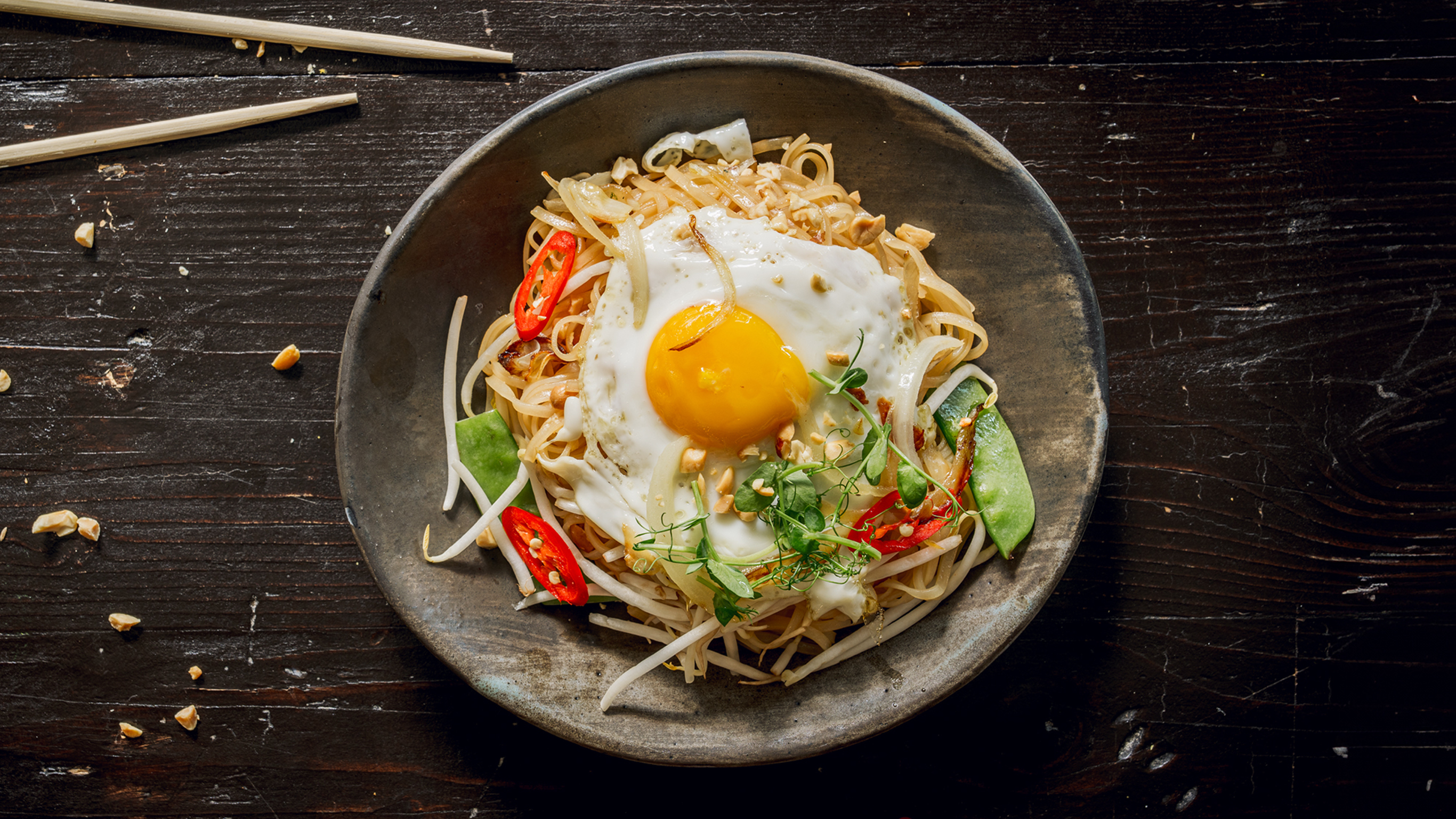 A plate of Pad Thai in a Flash with Sunny-side Up Eggs from the Centr menu sits on a table ready for eating.