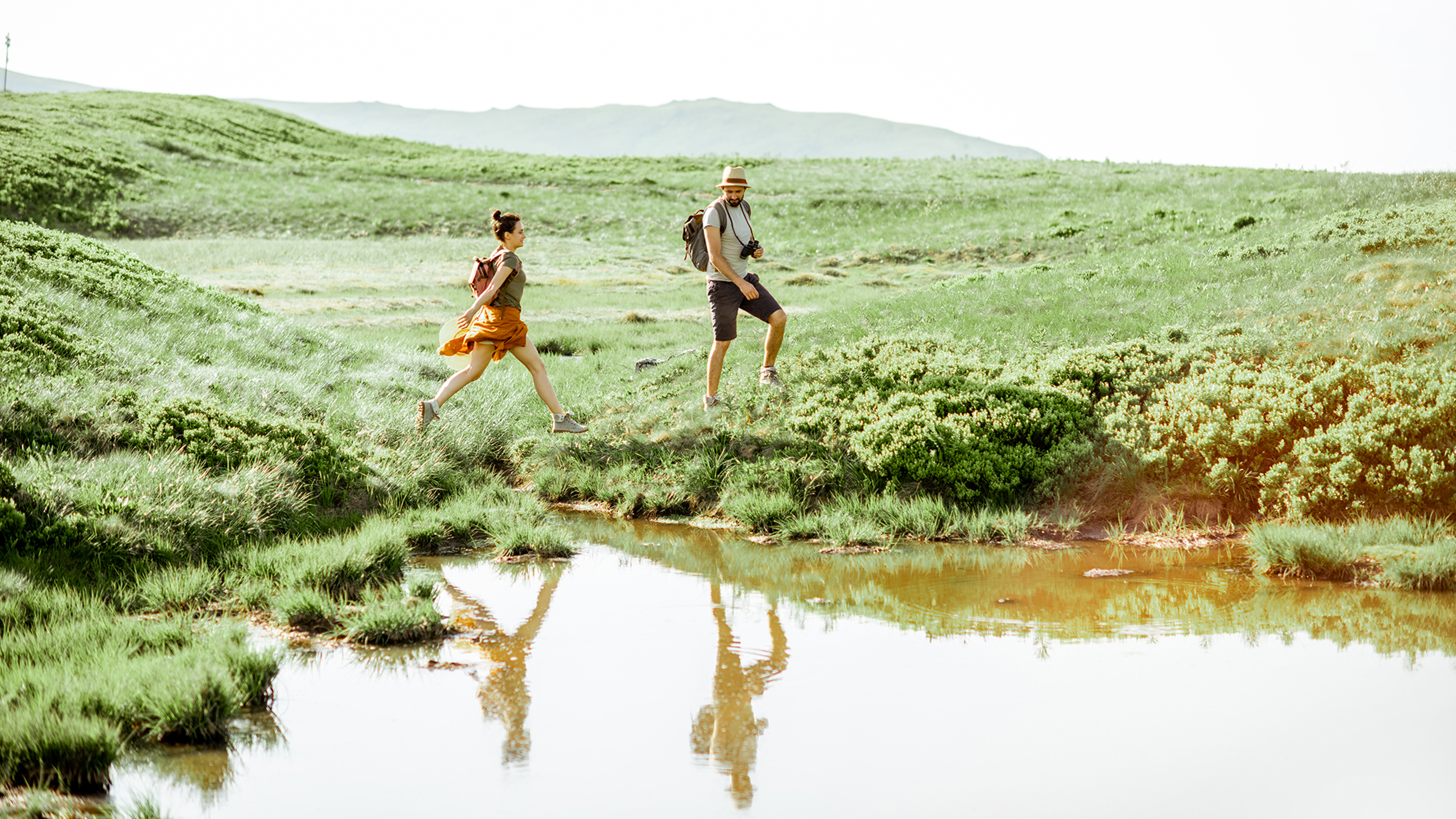 A man and a woman hike through a meadow.