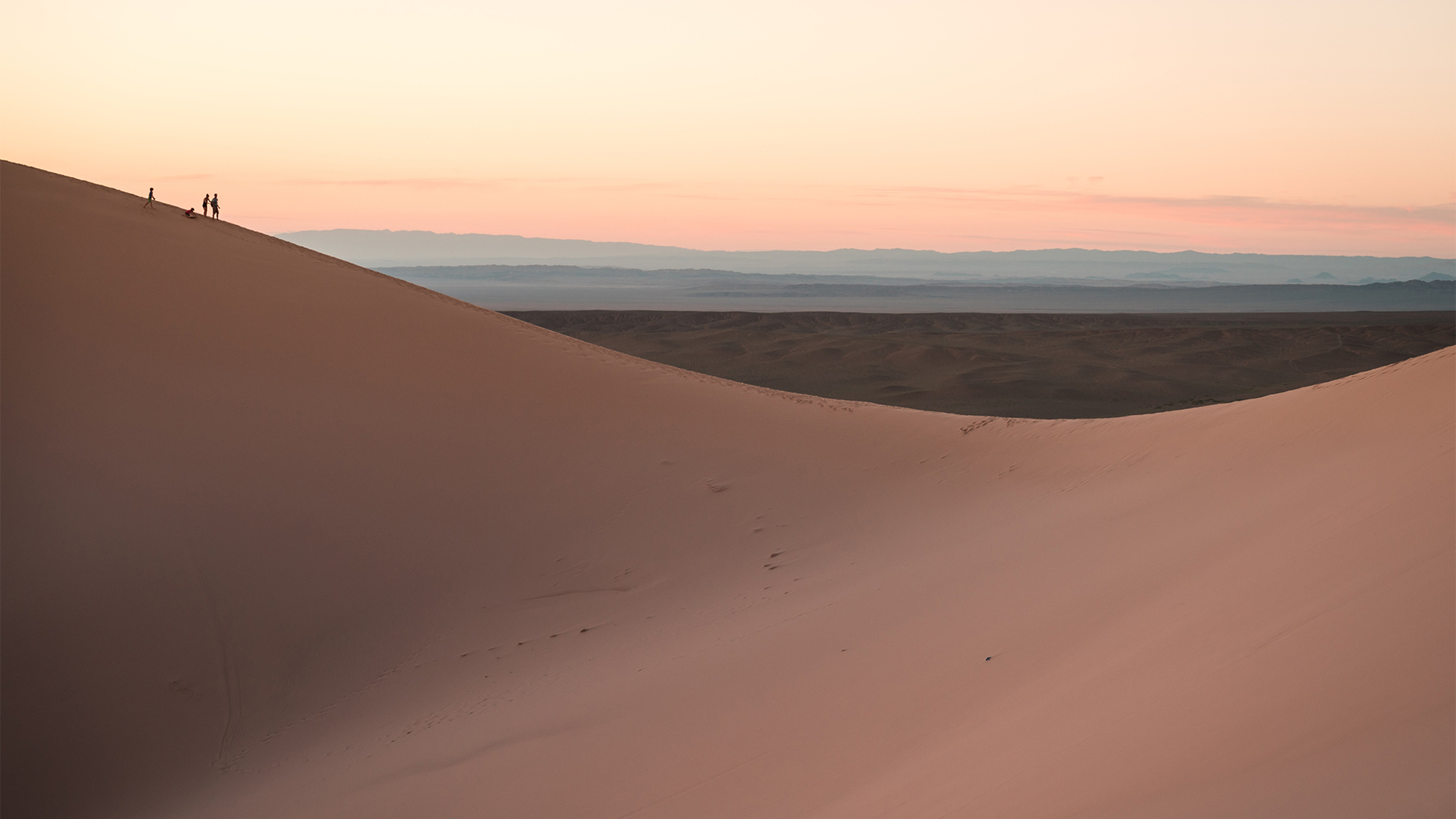An extra wide shot of people walking over sand dunes.